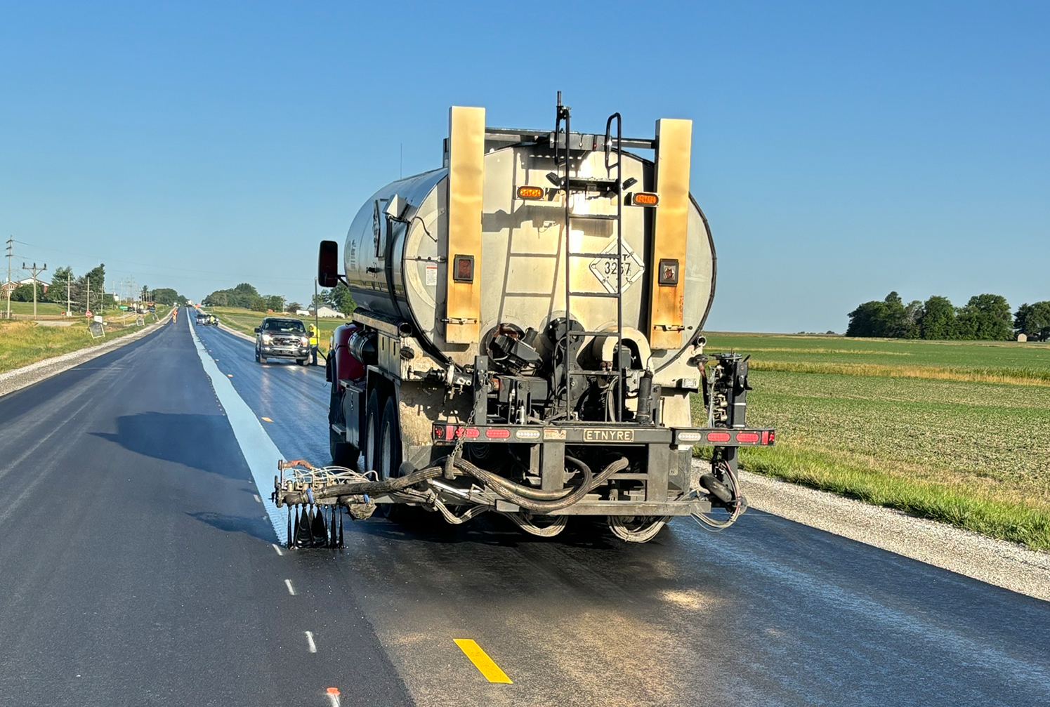 Paving truck drives down the road spraying a thing band of asphalt on the centerline