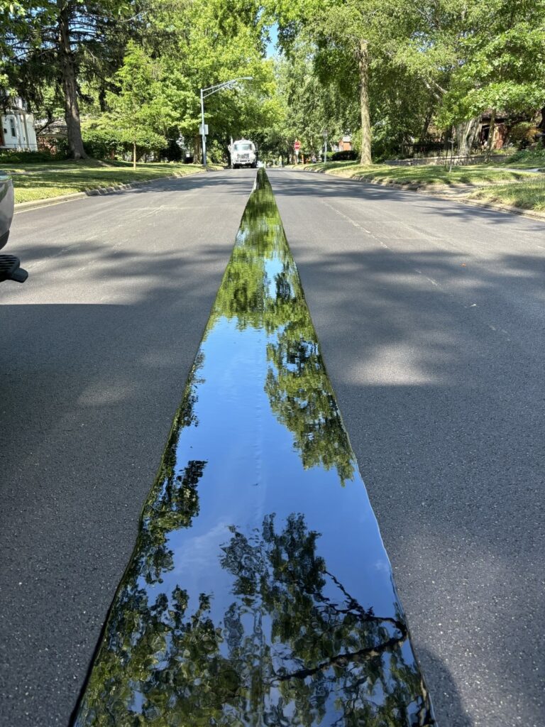 Evergreen Roadworks' application of J-Band on a road. The J-Band shows the reflection of the trees above