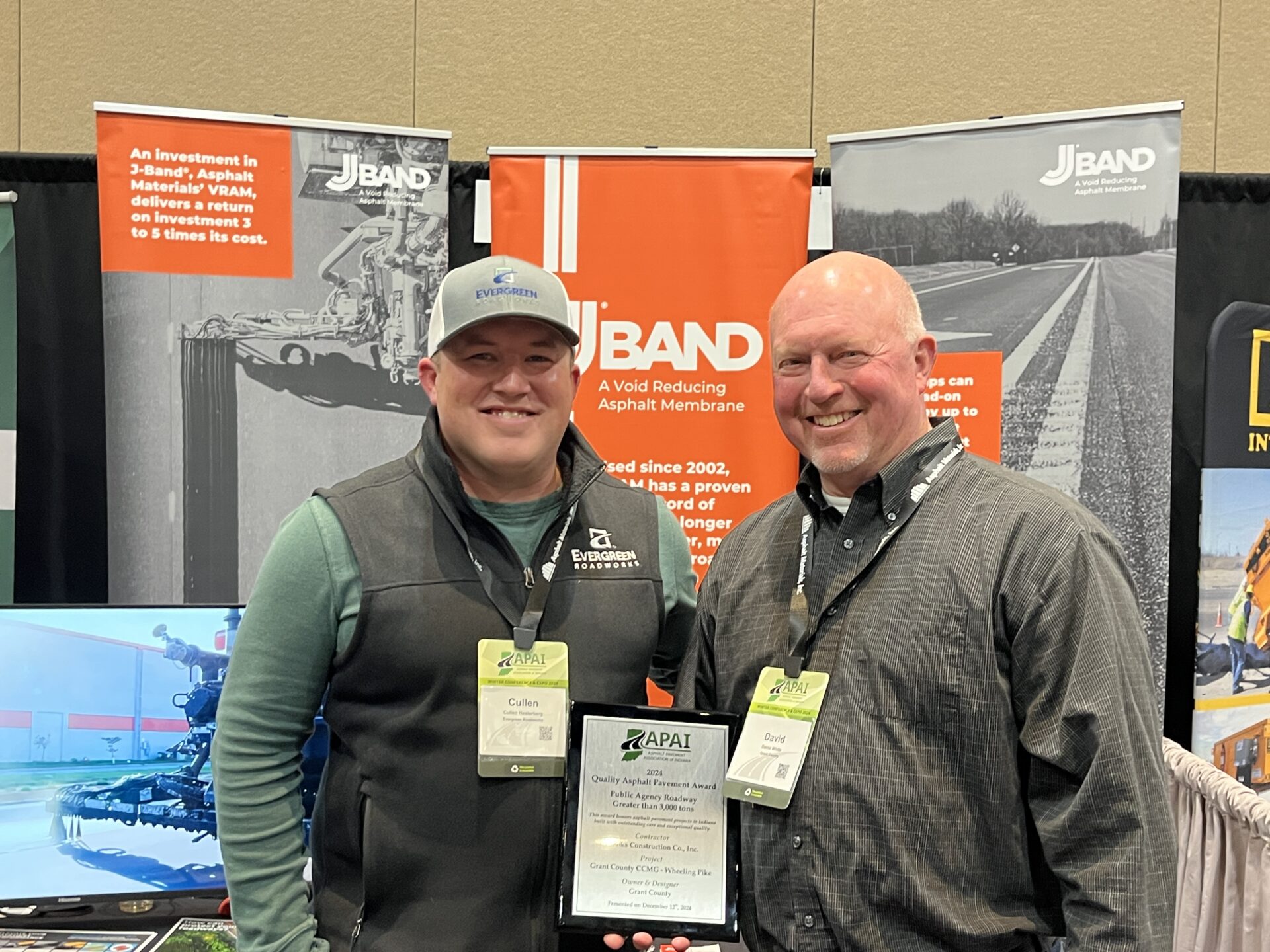 Two men pose with their award in front of Evergreen's trade show booth